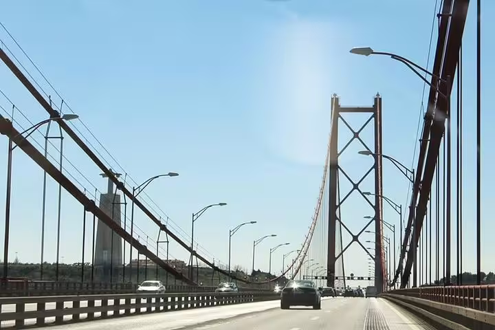 Driving over Lisbon's iconic 25 de Abril Bridge on a sunny day during a full-day private tour with custom stops in a premium vehicle.