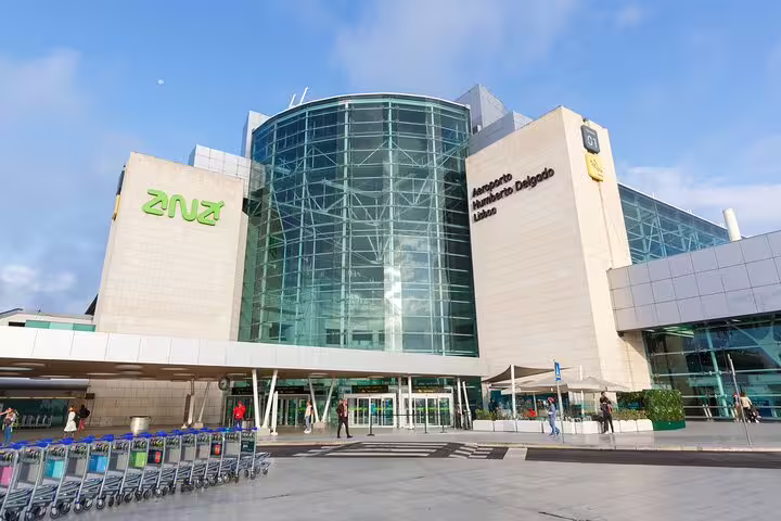 Modern glass facade of Lisbon Humberto Delgado Airport, ideal for private transfers to Lisbon Metropolitan Area, with trolleys ready.