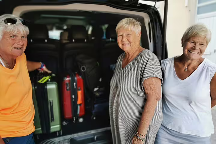 Three smiling travelers stand beside a Lisbon airport shuttle van with luggage, ready for a convenient and comfortable ride.