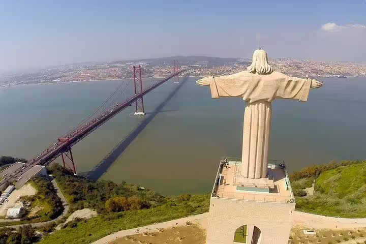 Aerial view of Lisbon's Cristo Rei statue overlooking the iconic 25 de Abril Bridge, perfect for airport transfer sightseeing tours.