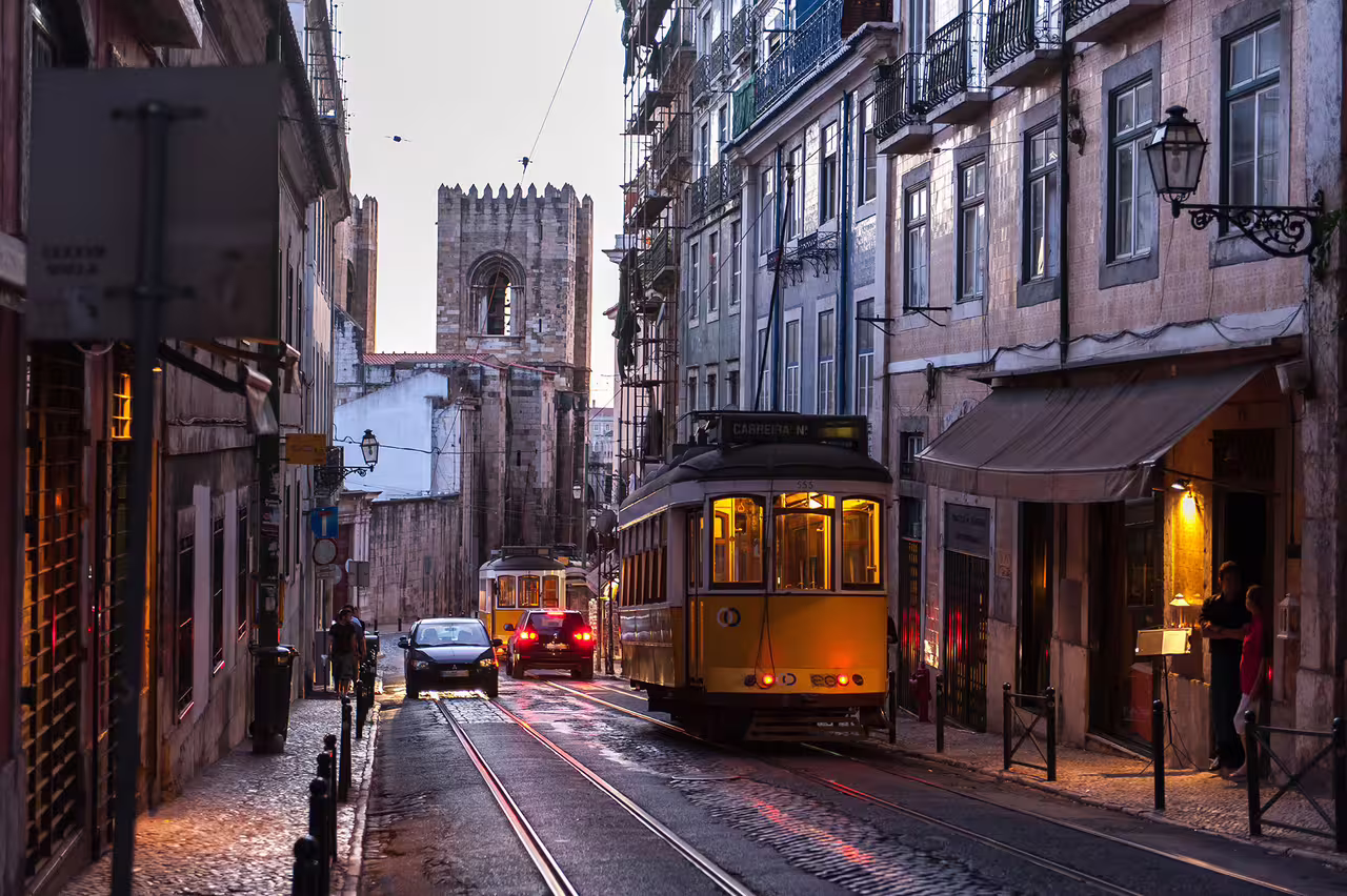 Yellow tram navigating a charming, narrow street in Lisbon's city center during sunset, perfect for private airport transfer.