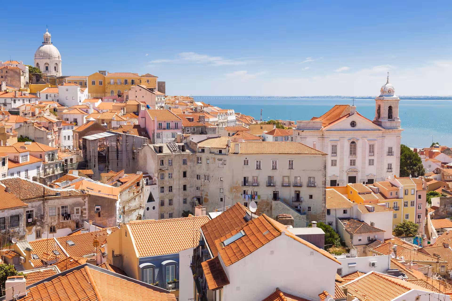 Scenic view of Lisbon's Alfama district with colorful rooftops and historic architecture overlooking the Tagus River.