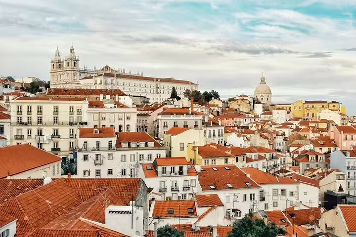 Panoramic view of Lisbon's Alfama district with historic architecture and iconic red rooftops on a sunny day.