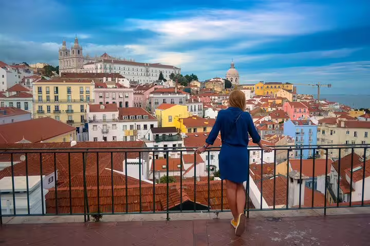 Woman in blue dress admires panoramic view of Lisbon's colorful Alfama district during a full-day private tour.