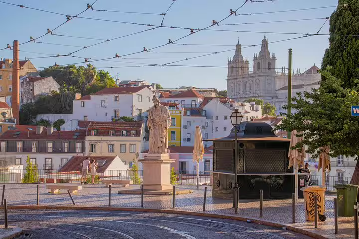 Scenic view of Lisbon's historic Alfama district with a statue, traditional architecture, and a glimpse of São Vicente de Fora.