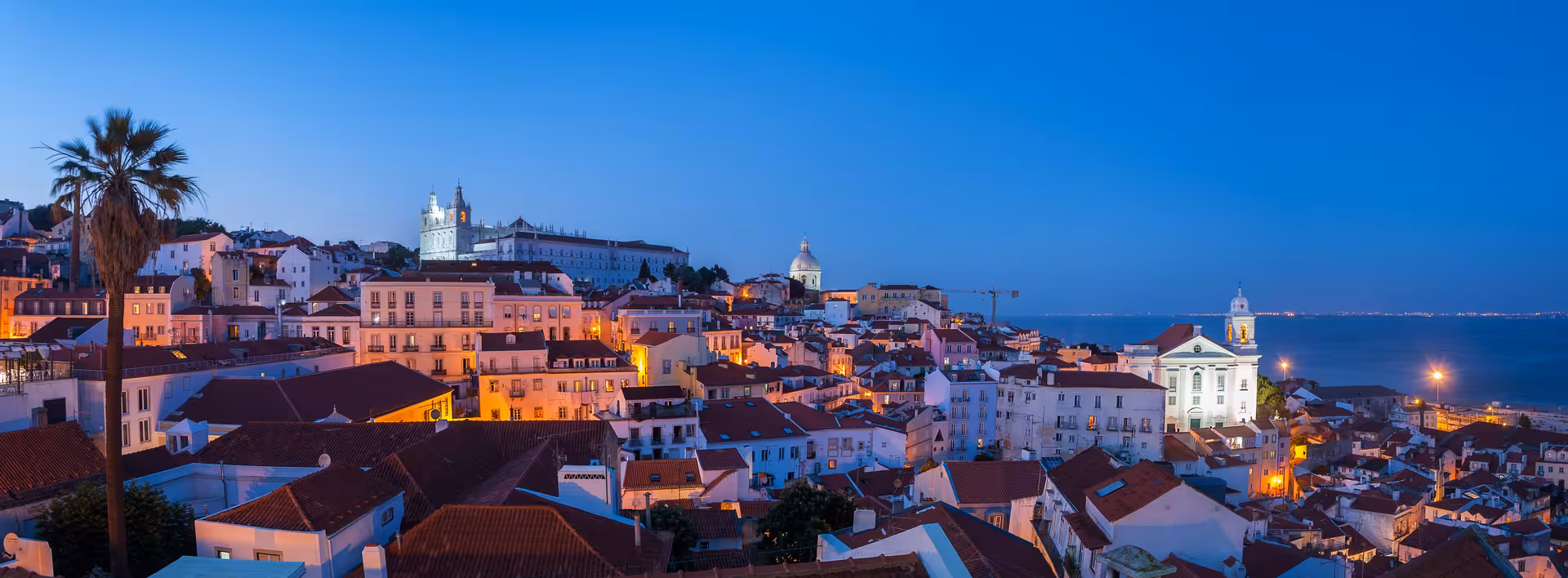 Scenic view of Lisbon's Alfama district at dusk with historic buildings and vibrant city lights.