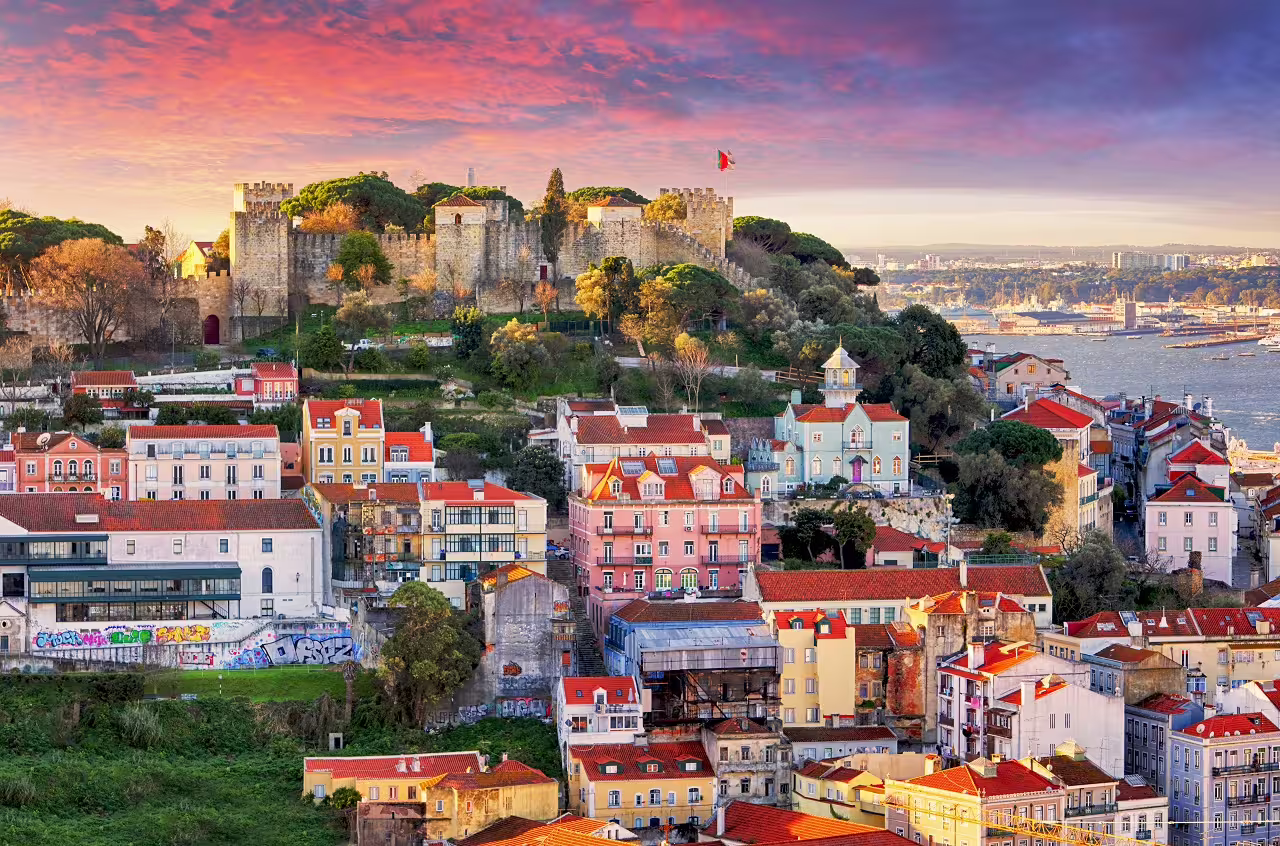 View of Lisbon's colorful Alfama district with São Jorge Castle at sunset, perfect for a 4-day cultural city break.