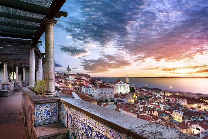 Scenic view of Lisbon's Alfama district at sunrise, showcasing historic architecture and vibrant cityscape by the Tagus River.