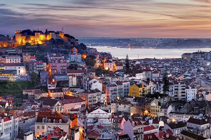 Sunset view over Lisbon's historic Alfama district with illuminated São Jorge Castle, capturing the city's vibrant charm.