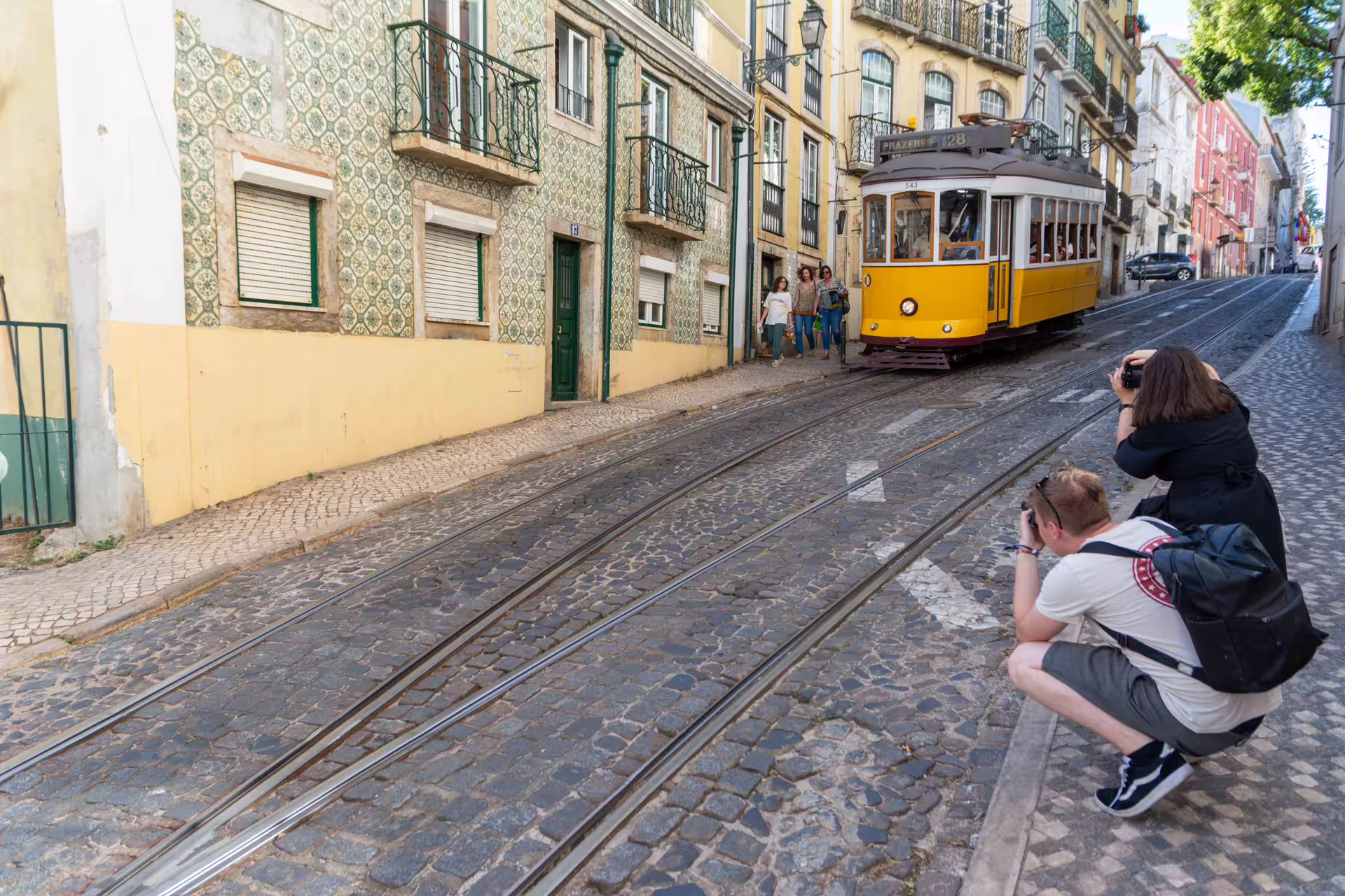 Photographers capture a classic yellow tram on a cobblestone street during the Alfama Photo Walk in Lisbon, led by a local expert.