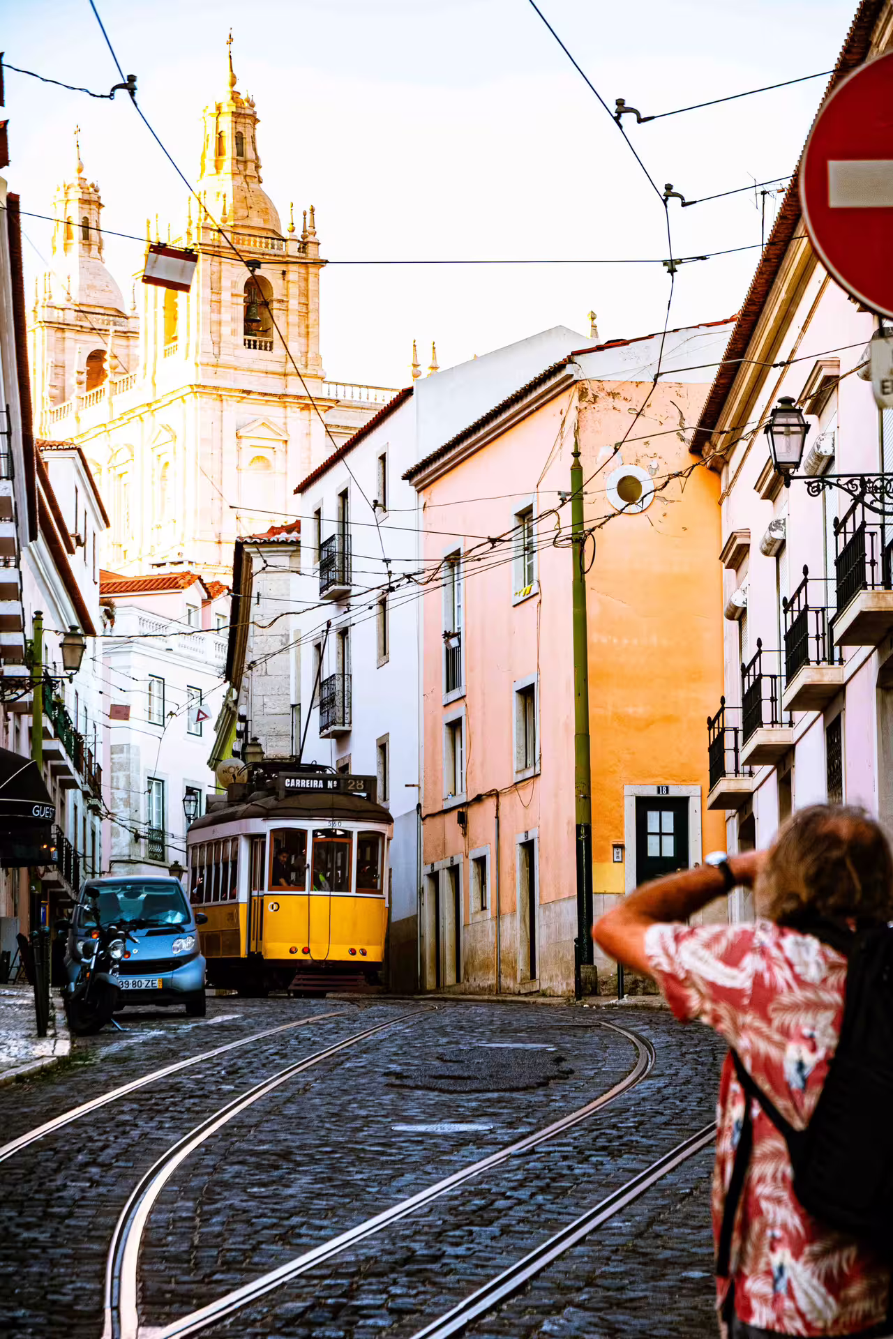 Photographer capturing a classic yellow tram and historic architecture during an Alfama photo walk in Lisbon at sunset.