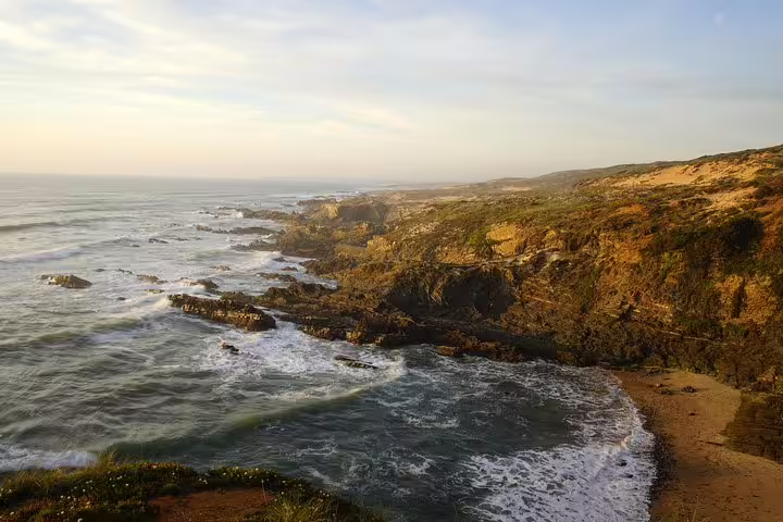 Scenic view of Portugal's rugged coastline on a Lisbon to Algarve tour, showcasing rocky cliffs and ocean waves at sunset.
