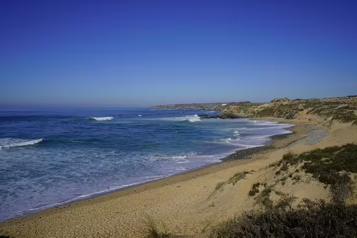 Scenic coastal view of a sandy beach with waves and cliffs on a Lisbon to Algarve tour, perfect for nature lovers.