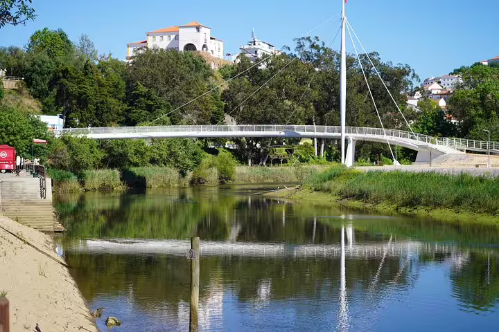 Scenic view of a modern pedestrian bridge over a lush river in Portugal, showcasing nature and architecture on the Lisbon to Algarve coastal tour.