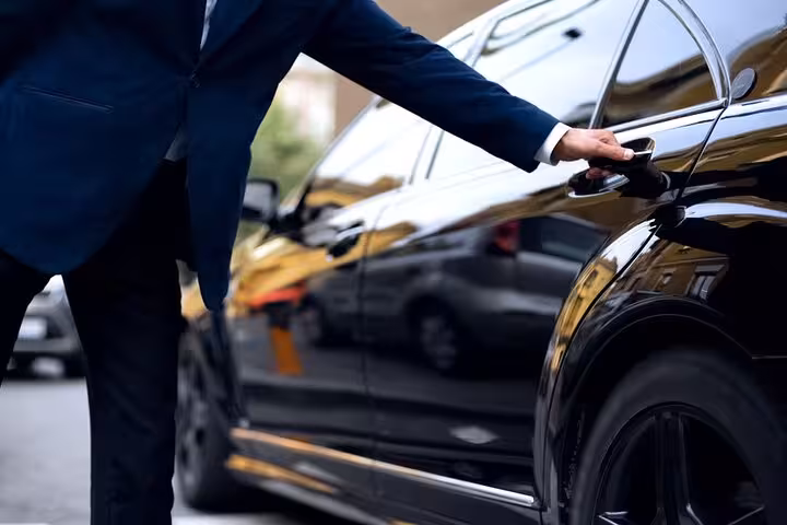 Chauffeur in a suit opens the door of a sleek black Mercedes for a private Lisbon to Algarve transfer.