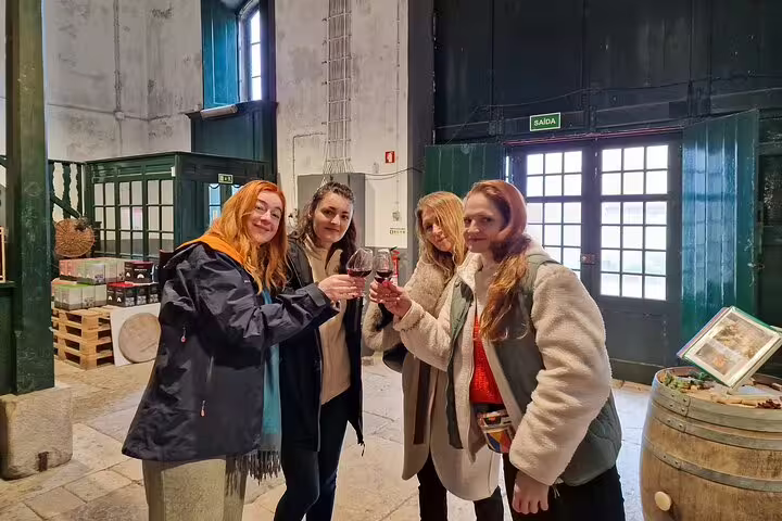 Group enjoying a wine tasting experience inside a rustic winery during a sightseeing tour in Arrabida from Lisbon.