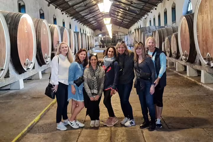 Group enjoying a wine tasting tour in a traditional Arrabida winery, surrounded by large wooden barrels and rustic charm.