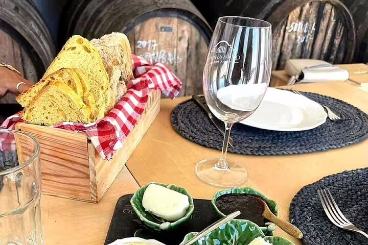 Rustic bread and wine glass on a table set for lunch during a Setúbal & Arrábida wine tour, with oak barrels in the background.