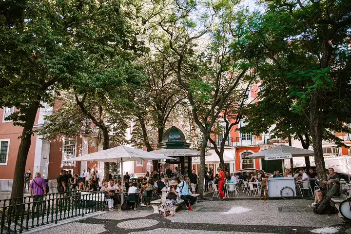 Bustling outdoor café under lush trees in Lisbon's lively Bairro Alto, perfect stop on a Chiado tuk tuk tour.