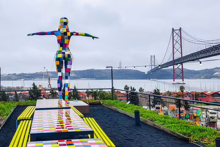 Colorful mosaic statue on Lisbon rooftop garden with 25 de Abril Bridge view, perfect for private bike tour exploration.