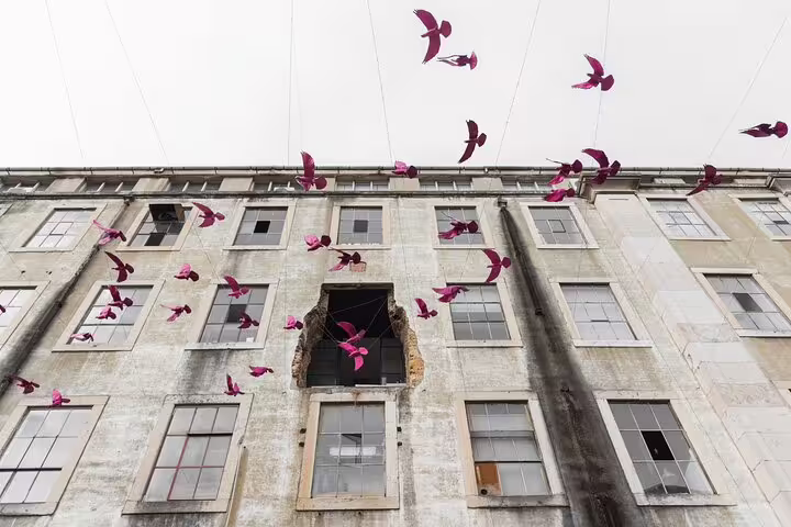 Pink bird sculptures soar above a historic Lisbon building, capturing the vibrant artsy vibe of the Lisbon & Belem bike tour.