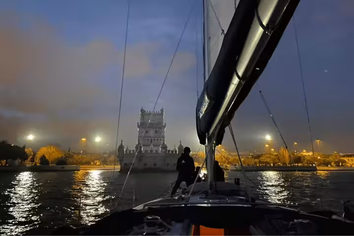 View of Lisbon's iconic Belém Tower illuminated at night from a sailing boat on the Tagus River during a scenic tour.