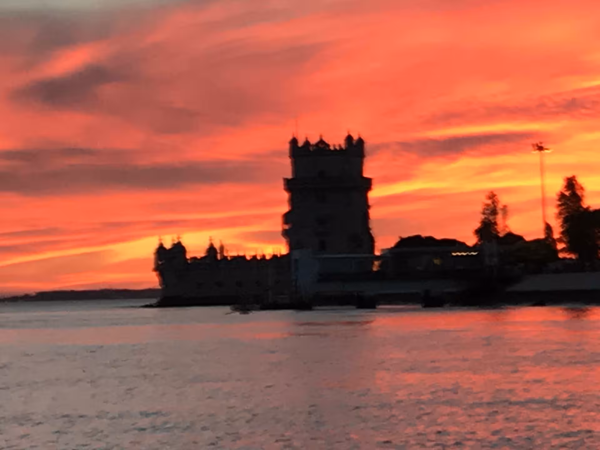 Belém Tower silhouette at fiery sunset on a Lisbon boat tour with wine on the Tagus River