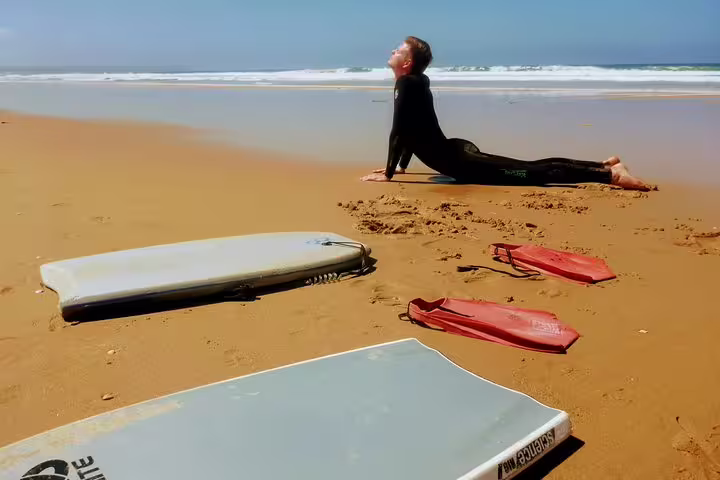 Person stretching on a sunny Lisbon beach with bodyboards and fins, ready for an exciting bodyboarding adventure.