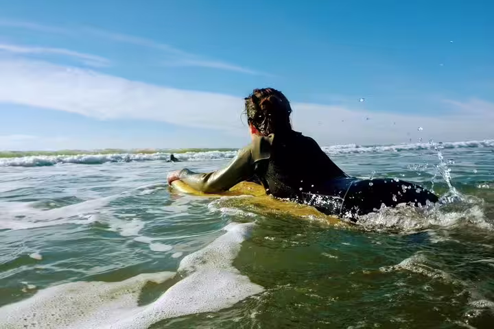 A person enjoys bodyboarding on the scenic Lisbon coast under a clear blue sky, highlighting an exciting water adventure.