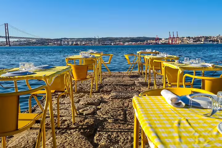 Outdoor dining setup with yellow tables and chairs overlooking the Tagus River, perfect for a Lisbon and Cacilhas food and drink tour.