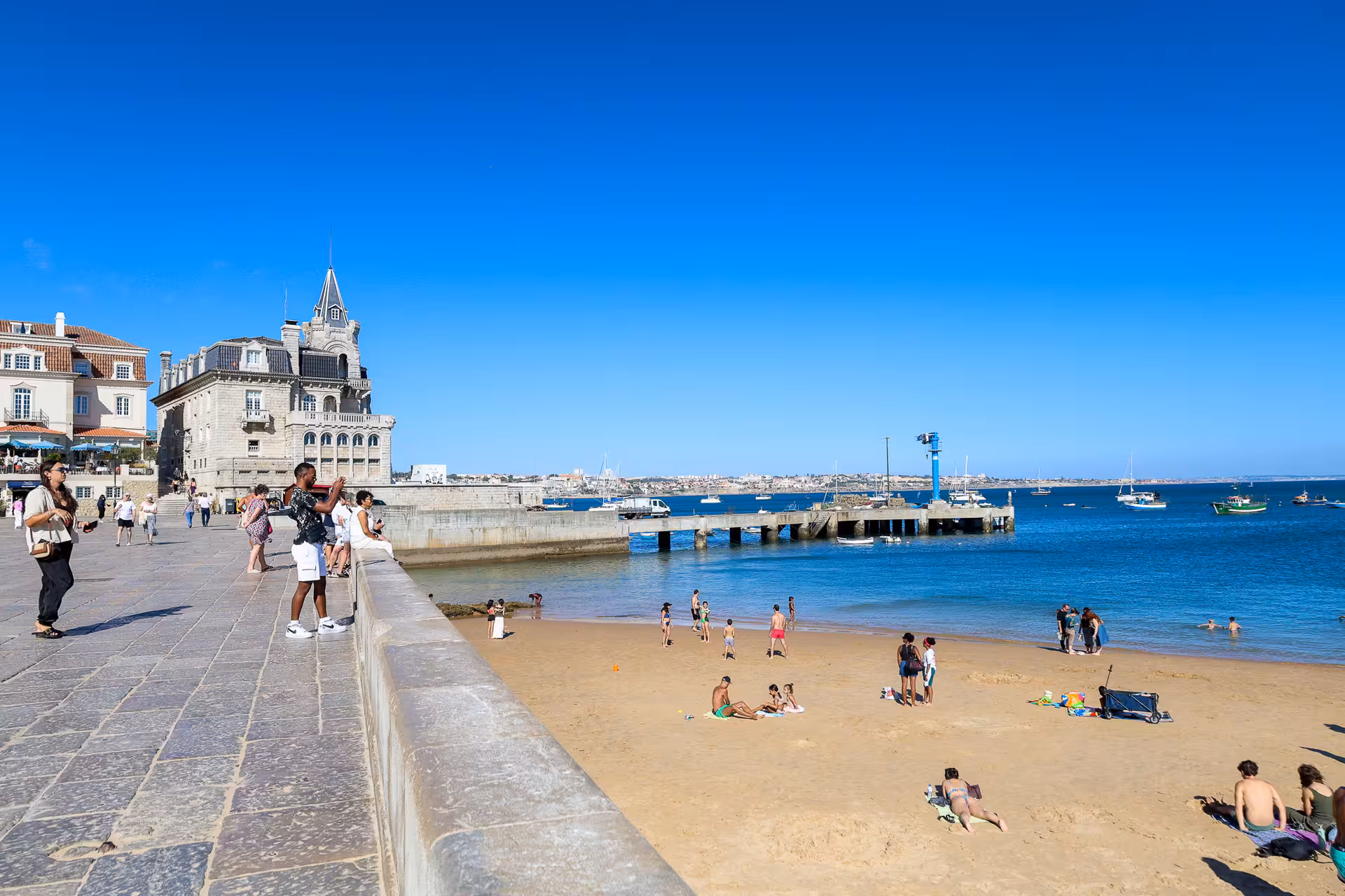 Tourists enjoy the sunny beach and historic architecture of Cascais during a Lisbon day tour.