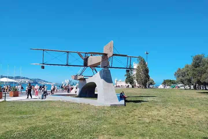 Monument of a historic seaplane in Lisbon, located by the waterfront with tourists exploring the area.