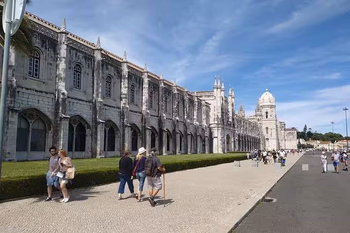 Tourists walk by the historic Jerónimos Monastery in Lisbon, showcasing its stunning Manueline architecture.