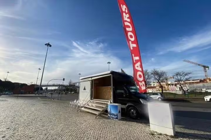 Mobile boat tour booking station in Lisbon with a large red flag, offering catamaran tours along the coast.