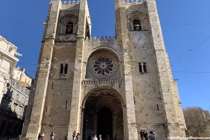 Front view of Lisbon Cathedral's gothic architecture basking in the sunlight with a deep blue sky backdrop.