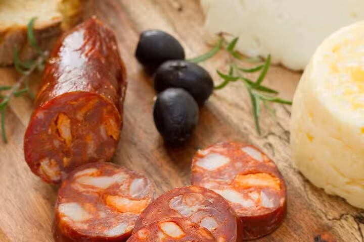 Sliced chorizo sausage with black olives and cheese on a wooden board, showcasing authentic Lisbon food tour flavors.