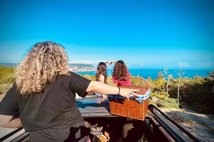 Tourists enjoy a scenic 4X4 Jeep ride with a picnic basket, overlooking the stunning Arrábida coastline near Sesimbra, Lisbon.