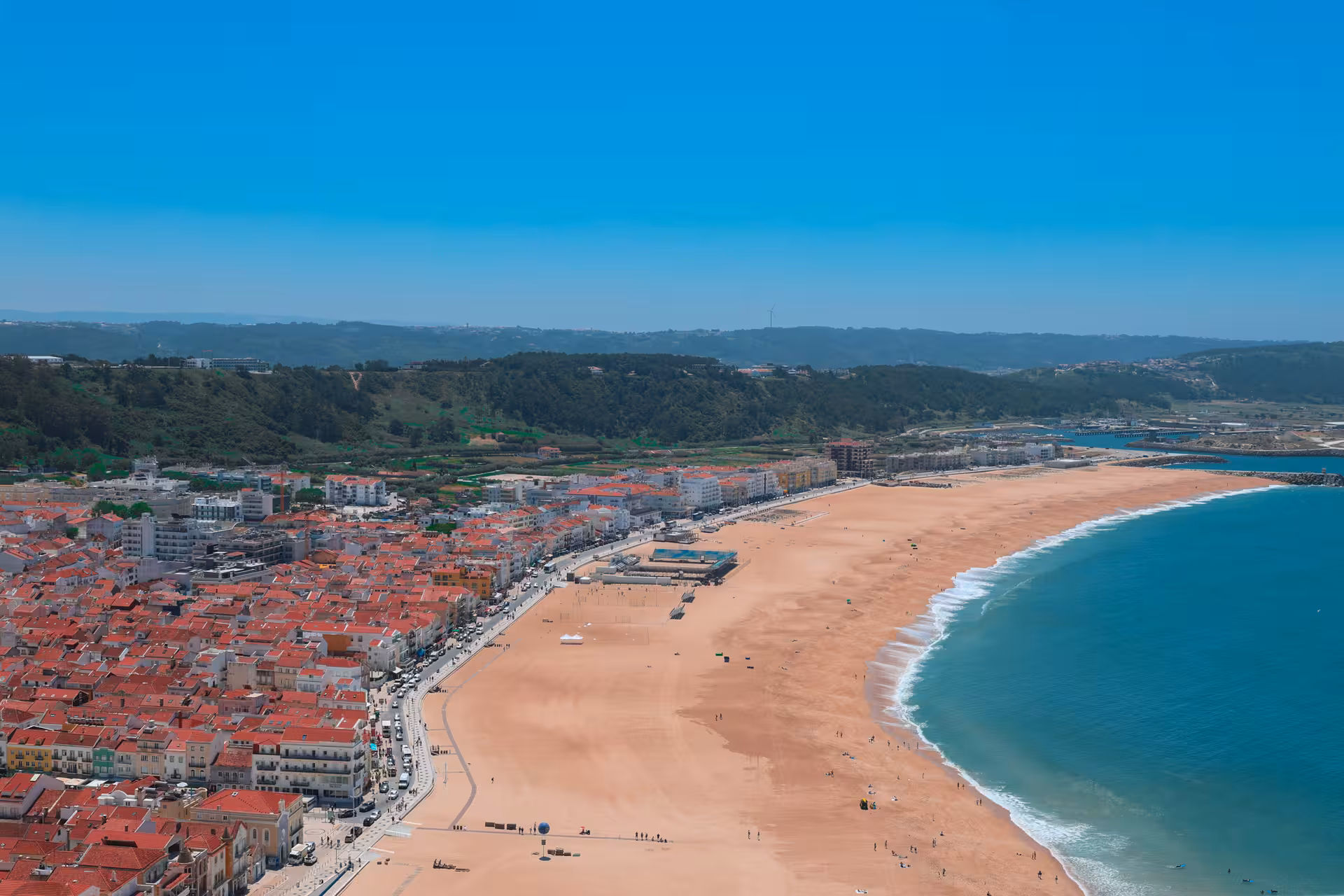 Aerial view of a picturesque coastal town with red-roofed buildings and expansive sandy beach near Lisbon.