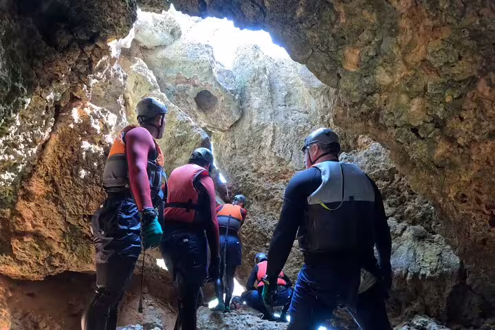 Explorers in wetsuits navigate through a rocky cave on a Lisbon coasteering and kayaking day trip.