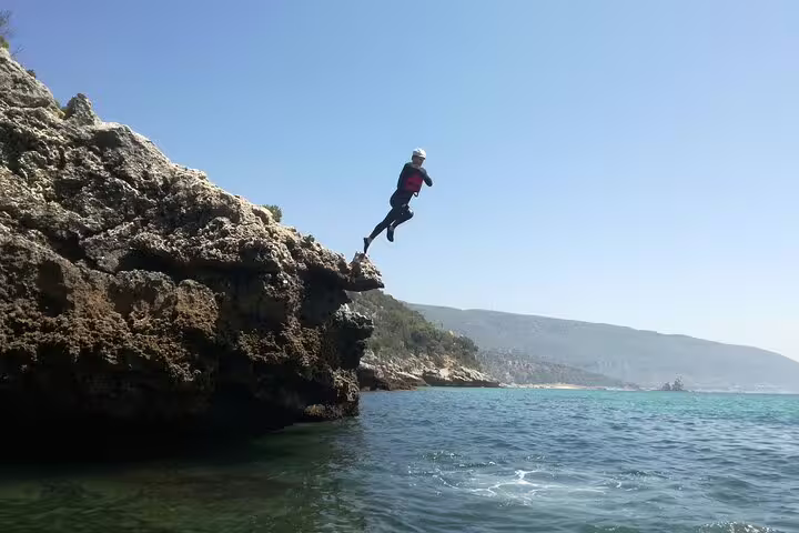 Adventurer leaps from a rocky cliff into the clear ocean during a Lisbon coasteering and kayaking tour.