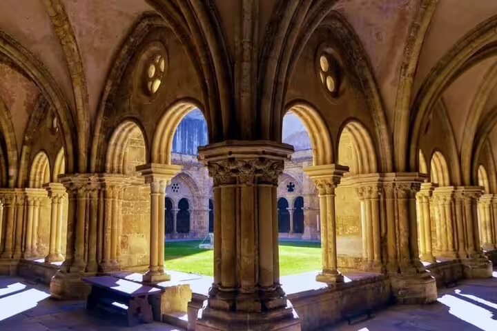 Historic cloisters in Coimbra bathed in sunlight, highlighting ornate arches on a private journey from Lisbon to Coimbra.