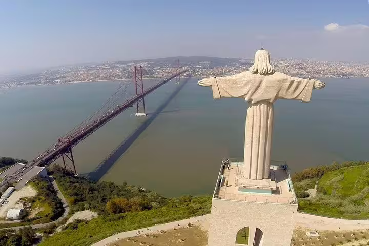 Aerial view of the Cristo Rei statue and 25 de Abril Bridge in Lisbon, showcasing iconic landmarks on a private city tour.