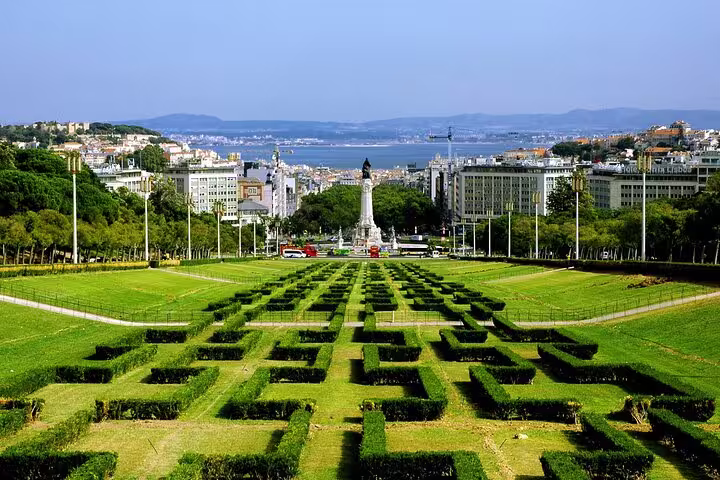 View of Lisbon's Eduardo VII Park with lush greenery, geometric hedges, and cityscape backdrop, featured in full-day tour.