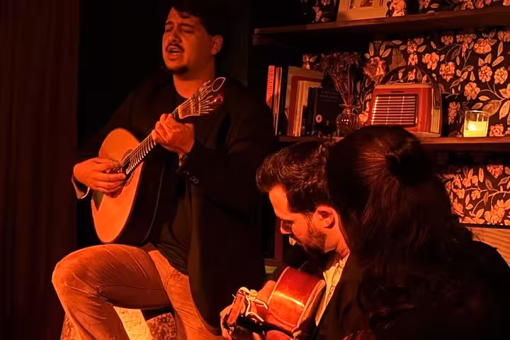 Musicians bowing with guitars in intimate Lisbon Fado concert setting, featuring warm lighting and cozy decor.