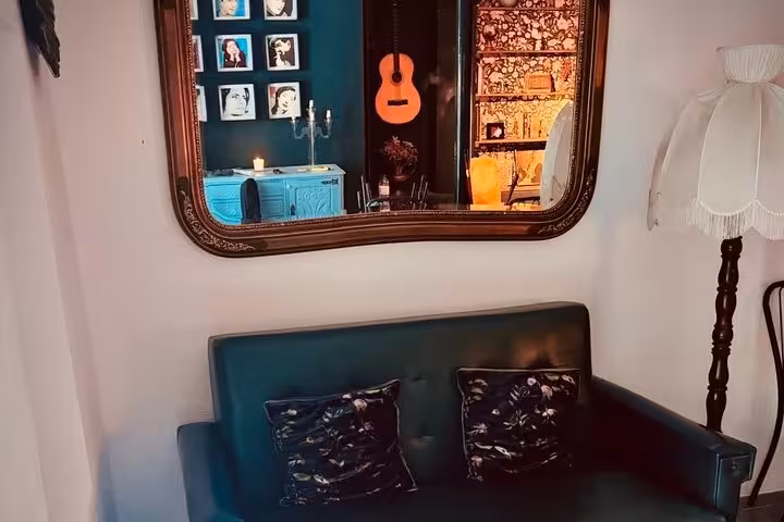 Chic Lisbon Fado venue with a stylish sofa, wall mirror reflecting guitar, and elegant candlelit decor.