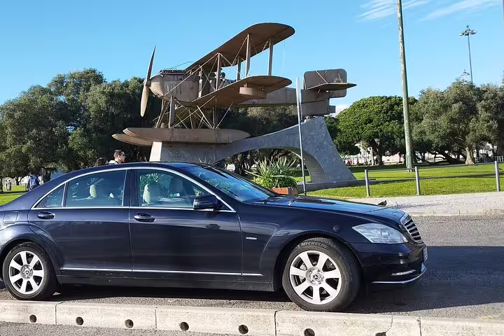 Luxury car parked near the iconic Santa Cruz biplane monument in Lisbon, showcasing the start of a Fatima and Conimbriga tour.