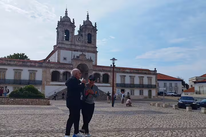 Tourists enjoying a scenic view of a historic church during a private full-day Fatima, Nazare, and Obidos tour from Lisbon.