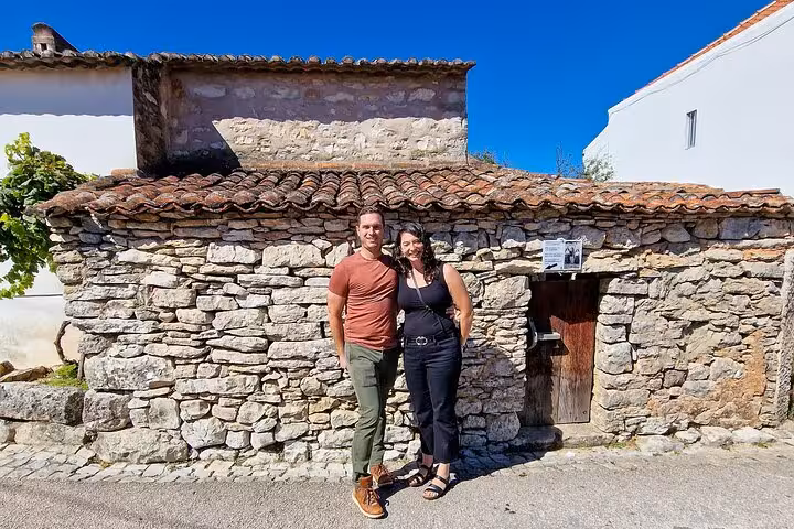 Travelers posing by a rustic stone house in Fatima on Lisbon to Fatima round-trip tour for WYD Lisbon 2023