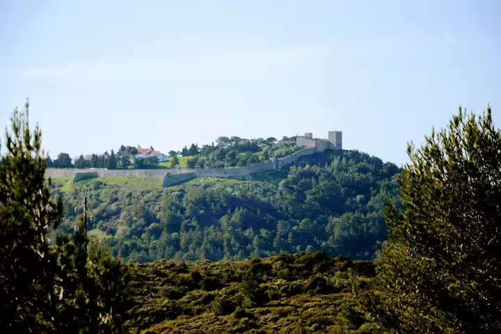Scenic view of a historic castle atop a lush hill near Lisbon, showcasing the natural beauty and cultural heritage of Portugal's south.