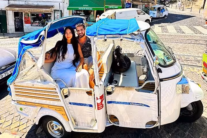 Couple riding a white tuk tuk on a 3-hour private Lisbon historic center tour through cobbled streets